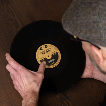 Man houdt een zwarte vinylplaat voorzichtig bij de randen vast voor het veilig bewaren en verzorgen van vinyl