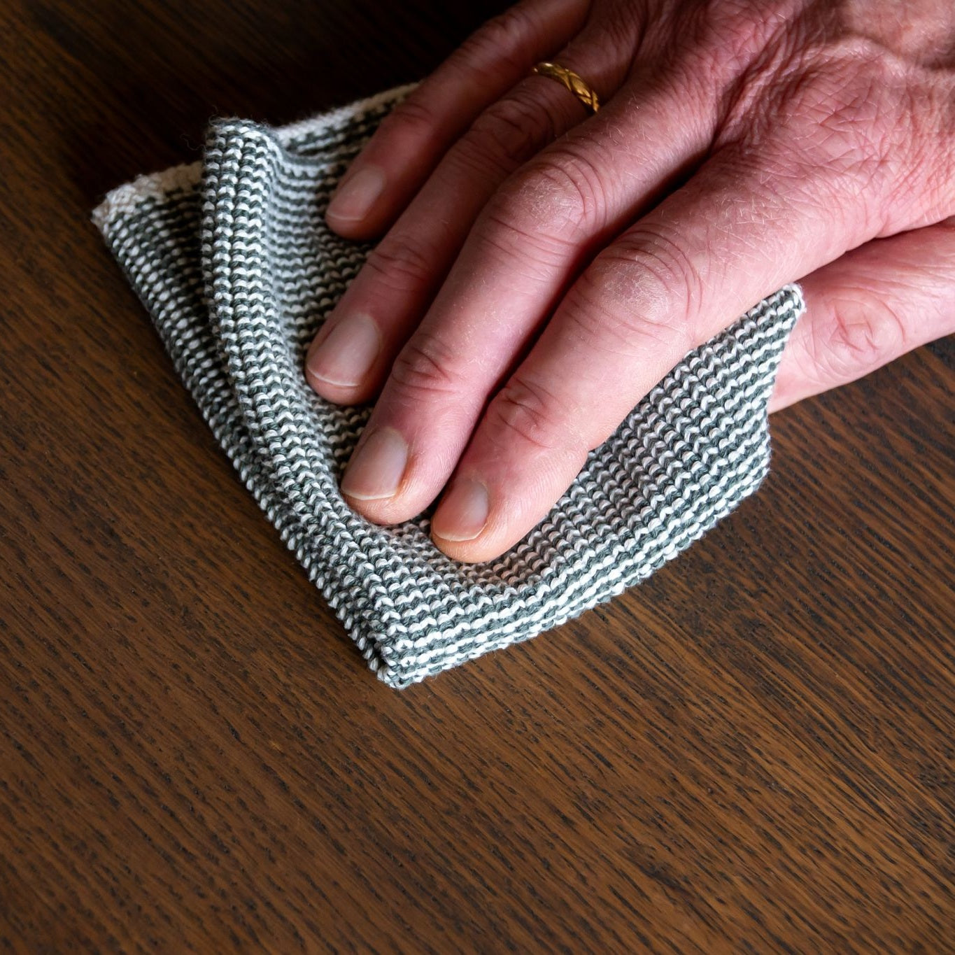 Handen reinigen het geoliede houten oppervlak van een platenkast voorzichtig met een zachte doek.