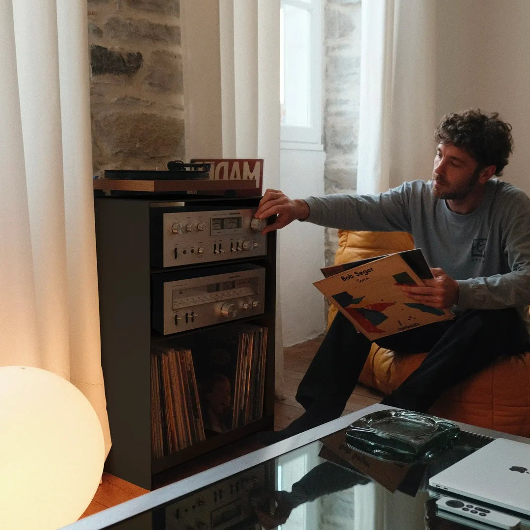 Vinylliefhebber kiest een lp naast de zwarte LOIA platenkast met platenspeler en vintage audioapparatuur