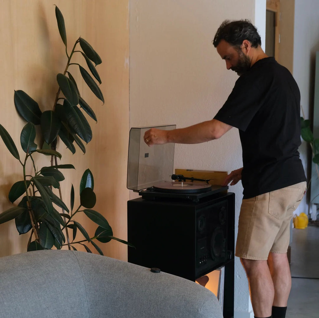 Vinylliefhebber legt een plaat op de platenspeler van de zwarte LOIA La Console Acier II